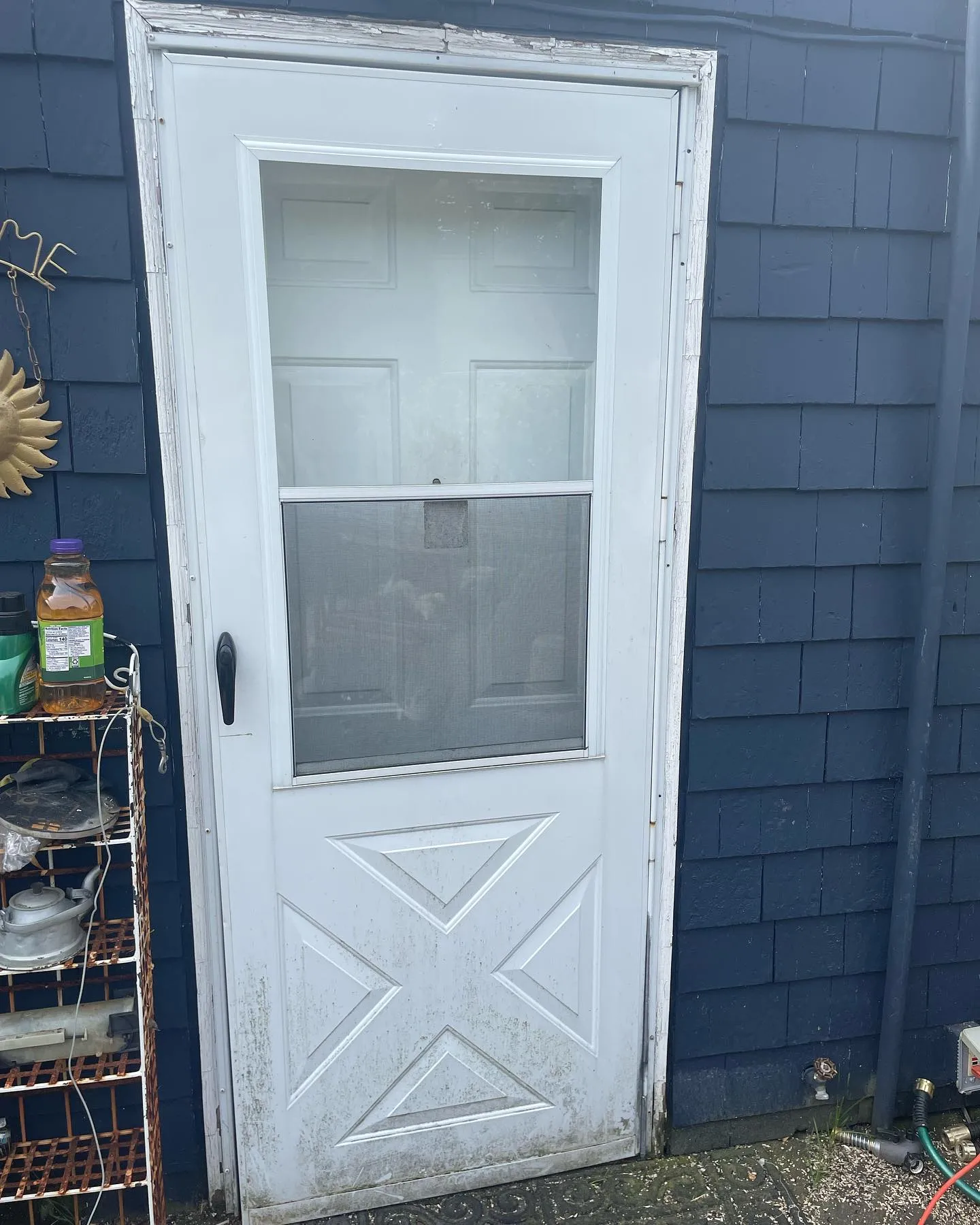 Before: the older storm door with a crossbuck lower panel at the blue-sided entrance.
