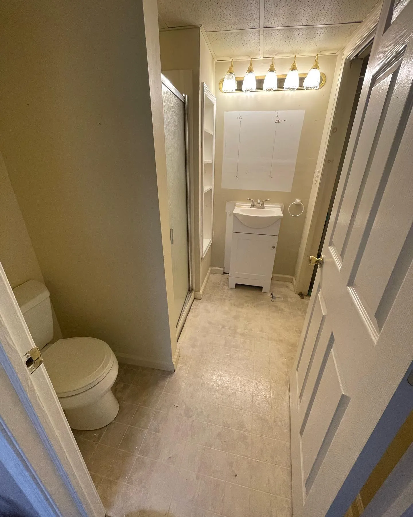 Before: the original bathroom with a compact vanity, light floor and existing shower enclosure.