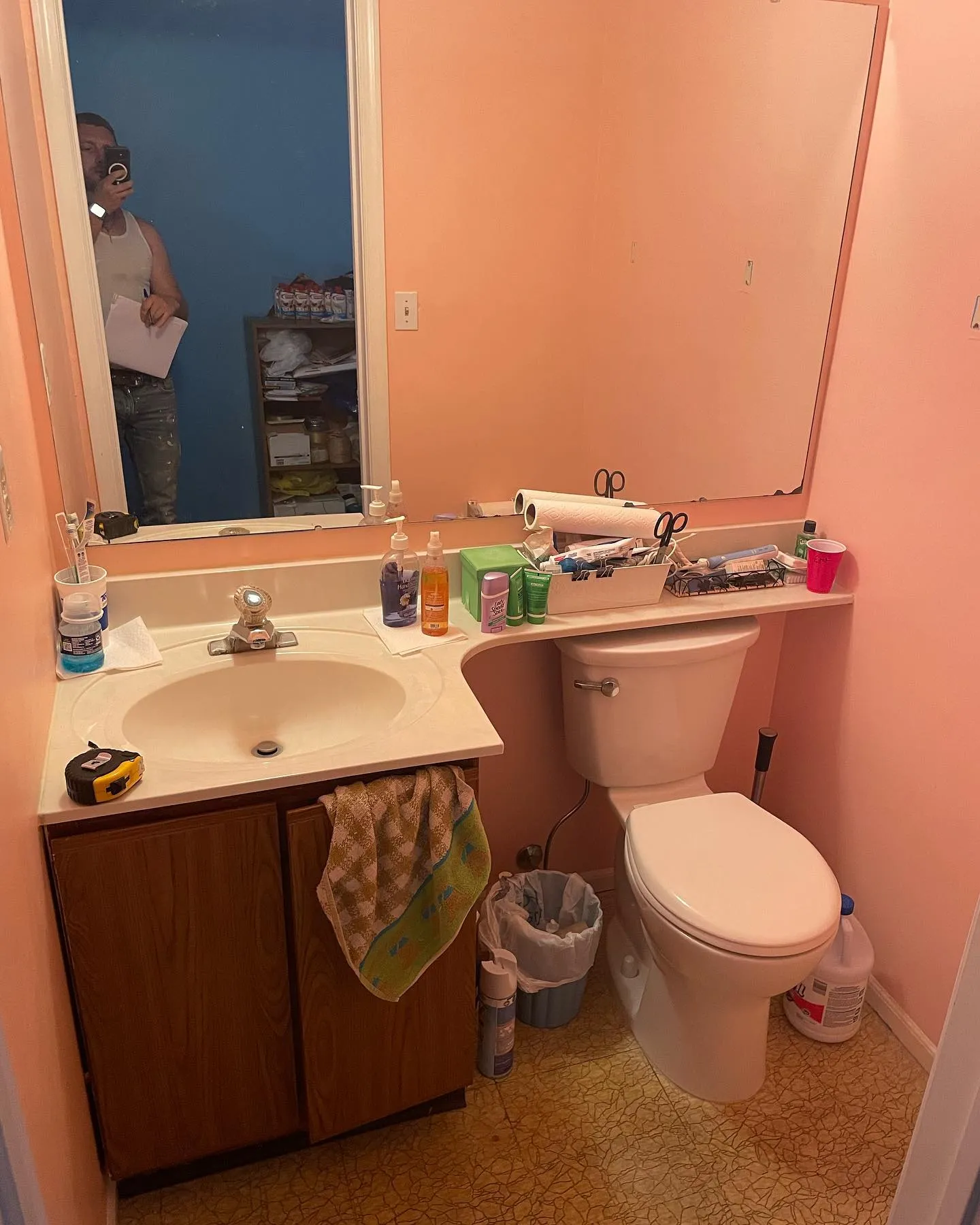 Before: the compact bathroom with peach walls, a wood vanity, a long countertop and the earlier toilet.
