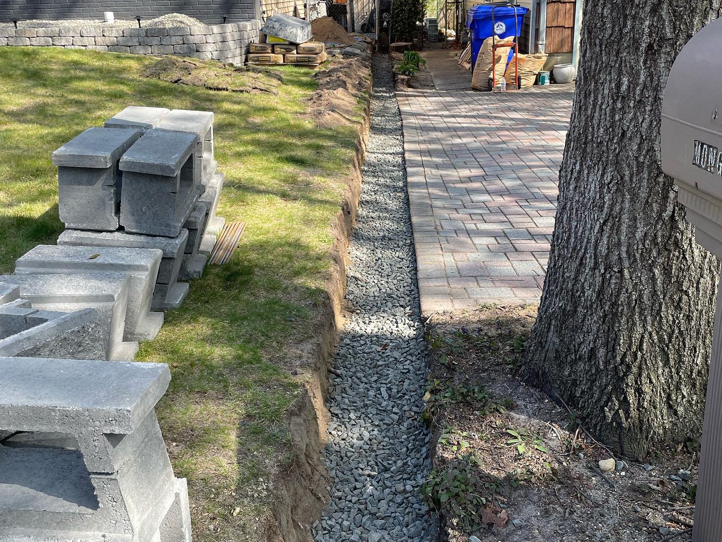 A view along the crushed-stone base toward the house, with the replacement blocks stacked nearby.