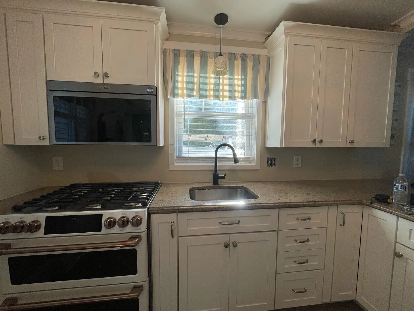 Before: the kitchen with its earlier cabinet finish, plain backsplash walls and original pendant light.