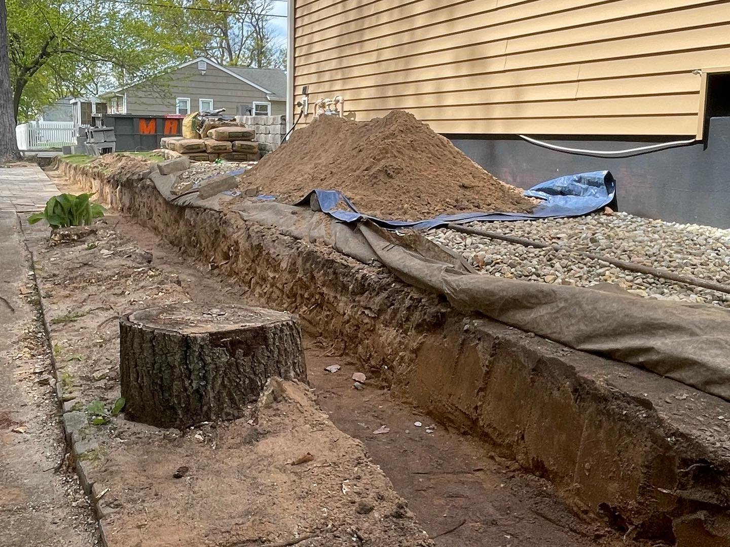 The side section after removal, showing the exposed ground, remaining tree stump and the existing gravel strip by the house.